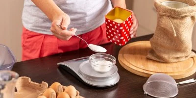 Člověk měří bílý prášek na váze v kuchyni s vejci vedle