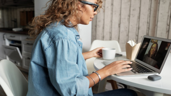 Žena sedí u počítače s notebookem pro online schůzku.