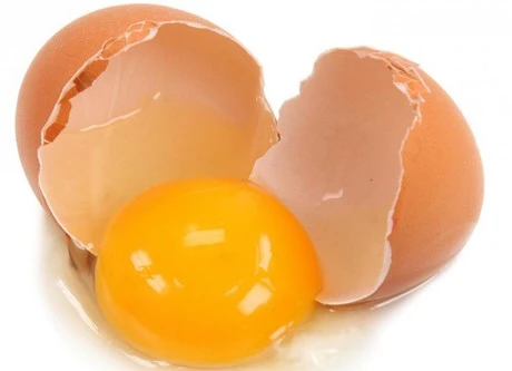 Rozbité vejce s žloutkem a kousky skořápky na bílém pozadí.