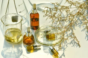Sklenice s olejem a suché rostliny na bílém pozadí.