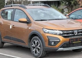 Oranžový automobil značky Dacia zaparkovaný na parkovišti.
