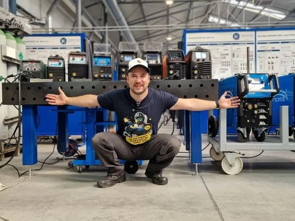 Muž mezi dvěma modrými zvarovými stroky v dílně.