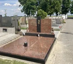 Červený granitový náhrobek s vyrytými jmény v hřbitově.