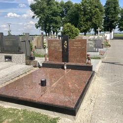 Červený granitový náhrobek s vyrytými jmény v hřbitově.