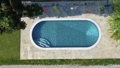 Pohled shora na soukromý bazén s ležáky a zelení.