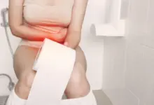 Žena sedí na záchodě s rukama přes bolavý žaludek.