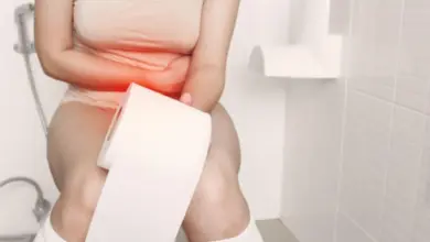 Žena sedí na záchodě s rukama přes bolavý žaludek.