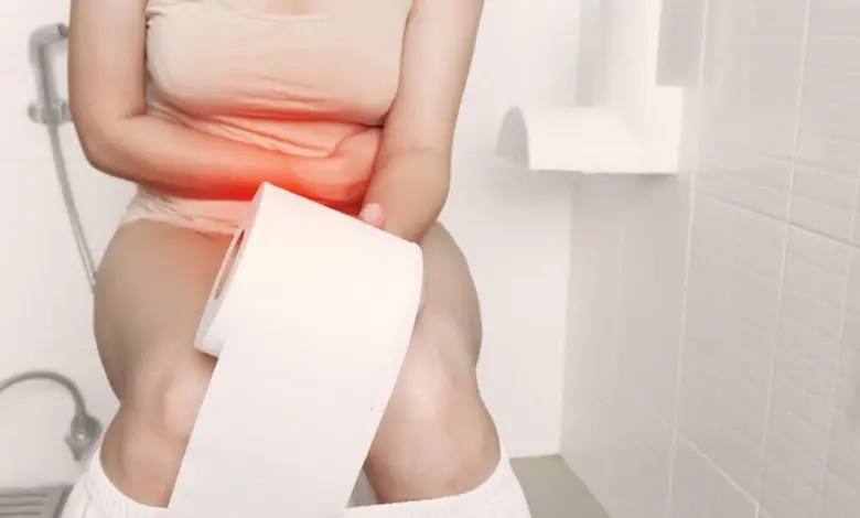 Žena sedí na záchodě s rukama přes bolavý žaludek.