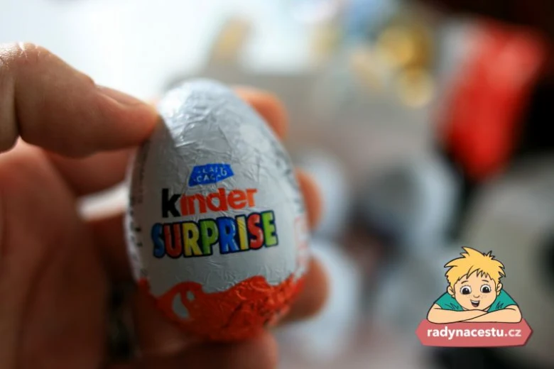 Ruka drží čokoládové vajíčko Kinder Surprise s barevným logem.