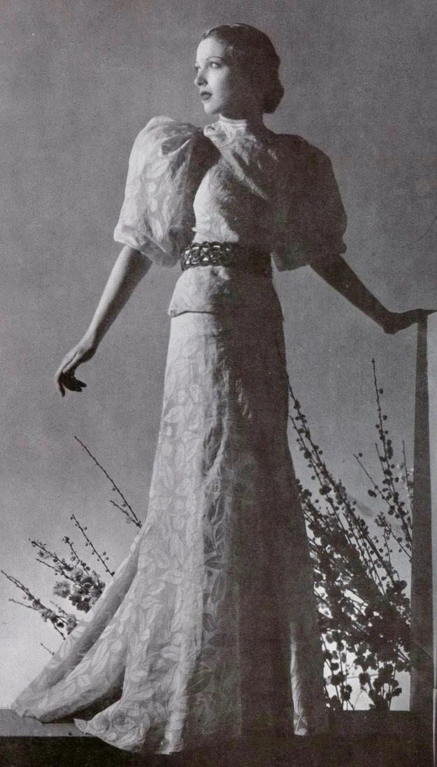 Žena v módním šatu z roku 1940 s květinovými větvičkami.