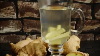 Sklenička s čajem zázvoru vedle kořenů zázvoru na tmavém povrchu.