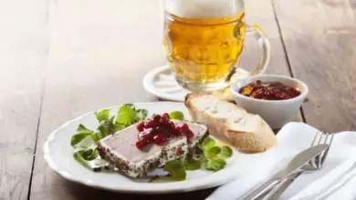 Kousek masa s brusinkami, chlebem a pivem na dřevěném stole.