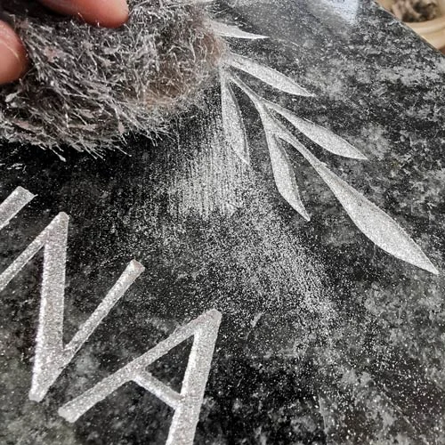 Ruční gravírování jména a listů do černého granitu pro náhrobek.