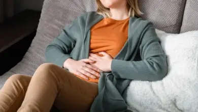 Žena sedí na gauči a drží si břicho v bolesti.