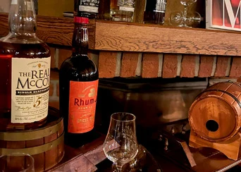 Dva lahve whisky a rum na dřevěných sudech před krbem.