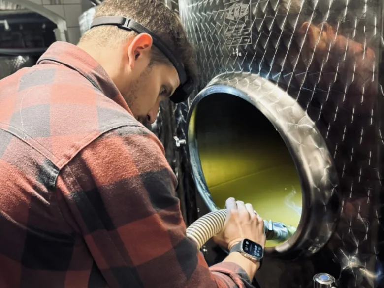 Winemaking worker handling wine clarification in industrial tank.