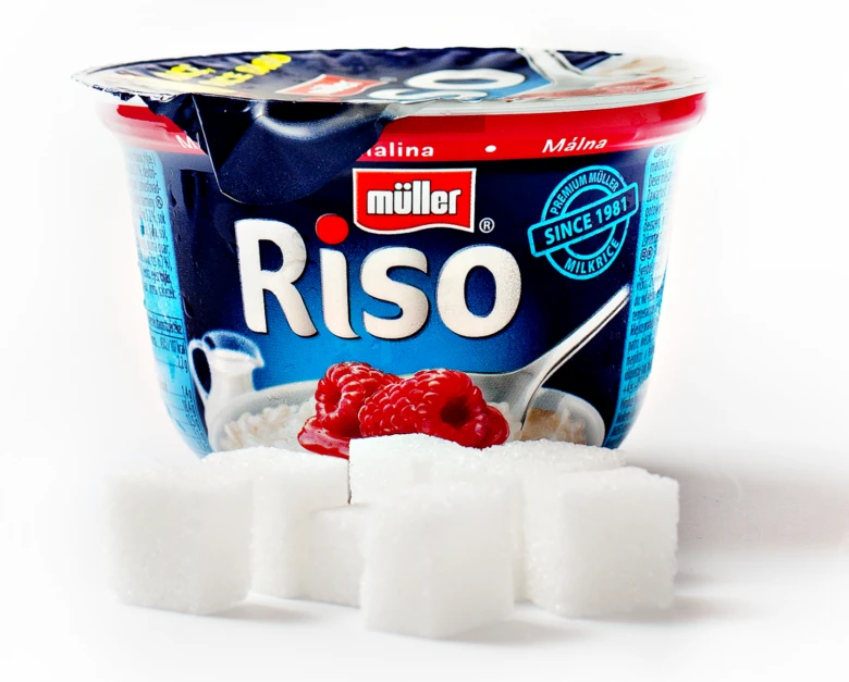 Jogurt s malinami vedle bílých kostek cukru na bílé pozadí.