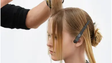 Kadeřník stříhá blond ženě účes v kadeřnickém salónu.