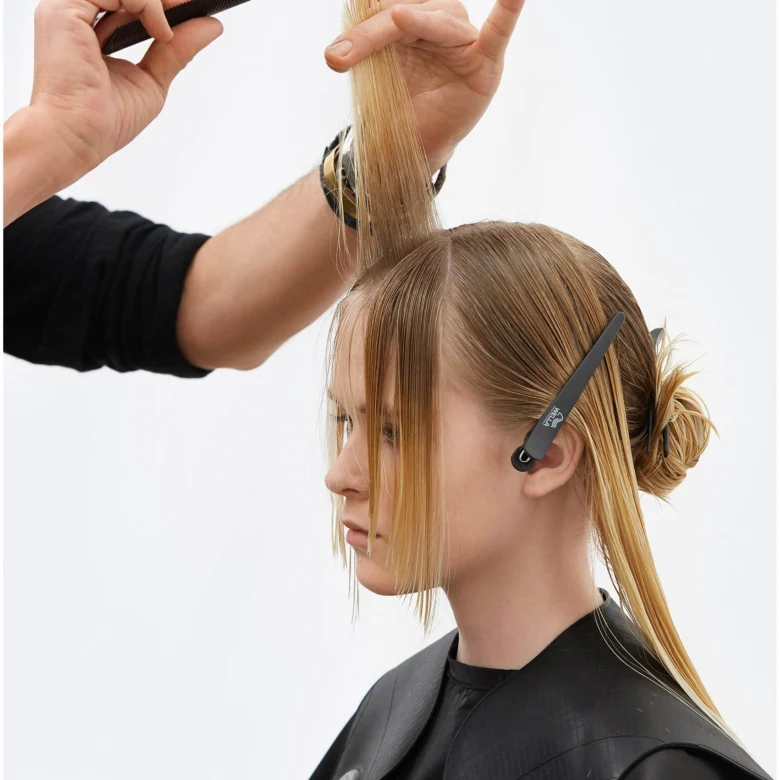 Kadeřník stříhá blond ženě účes v kadeřnickém salónu.