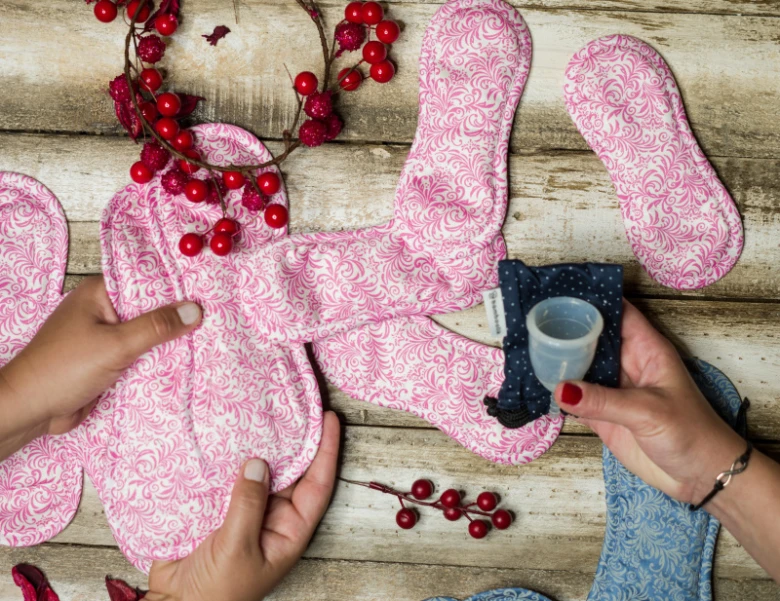 Ručníky, tampony a pohárek pro menstruaci na dřevěném povrchu