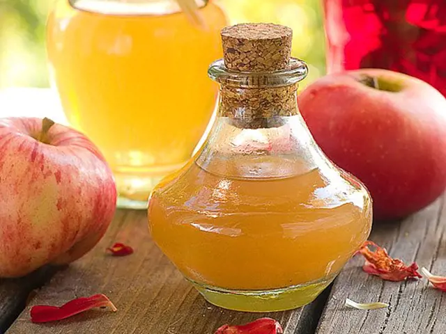 Sklenička jablkového octu s čerstvými jableky na dřevěném povrchu.