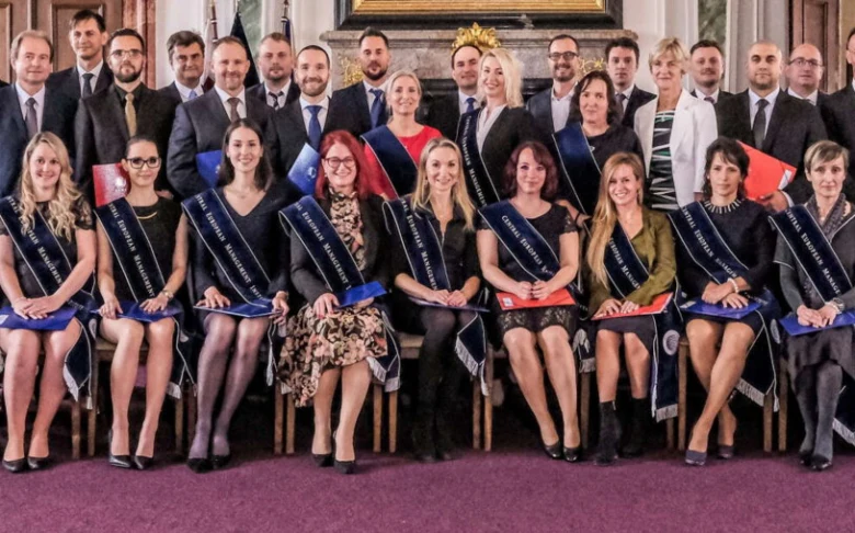 Skupina absolventů v šatech na formální fotografii.