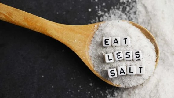 Dřevěná lžíce s solí a písmeny Eat Less Salt.