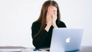 Stresovaná žena zakrývá tvář rukama u počítače.