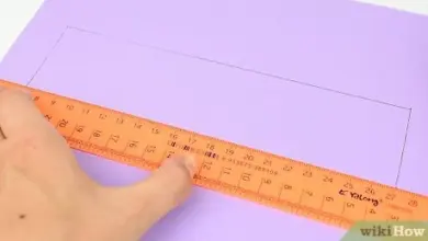 Ruka měří fialový papír oranžovou pravítkem pro výrobu kostky.