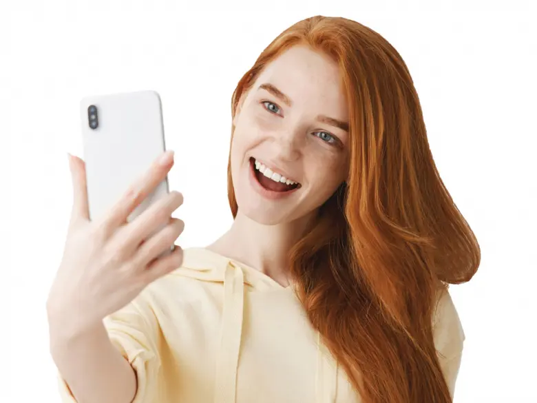 Smějící se žena s červenými vlasy pořizuje selfies na mobil.