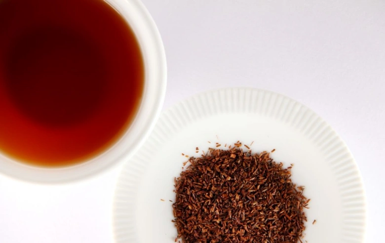 Suchá rostlinná surovina Rooibos čaj v šálku s naloženým nálevem.