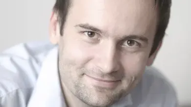 Muž se usmívá na kameru v bílé košili.