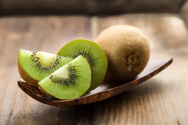 Dva nakrájené zelená kiwi s celým kouskem na dřevěném talíři.