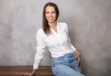 Usměvavá žena v bílé košili hledí do kamery.