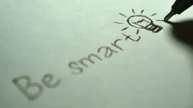 Ruka píše na papíře slova Be smart s kresbou žárovky.