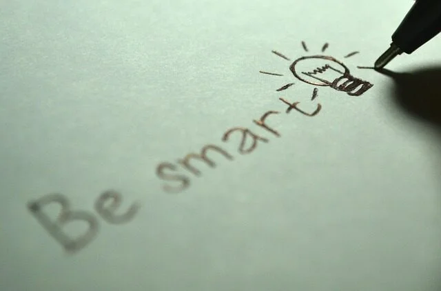 Ruka píše na papíře slova Be smart s kresbou žárovky.