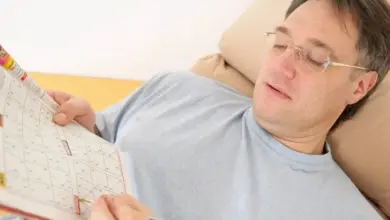 Muž řeší sudoku v časopisu, zatímco leží na gauči.