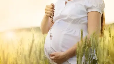 Těhotná žena modlí za zdravé dítě s růžencem v poli.