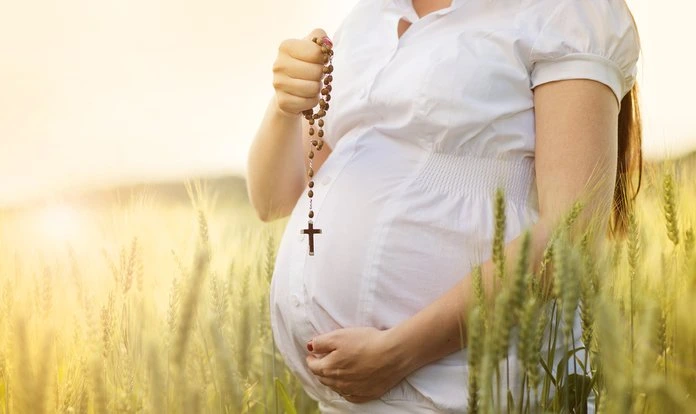 Těhotná žena modlí za zdravé dítě s růžencem v poli.