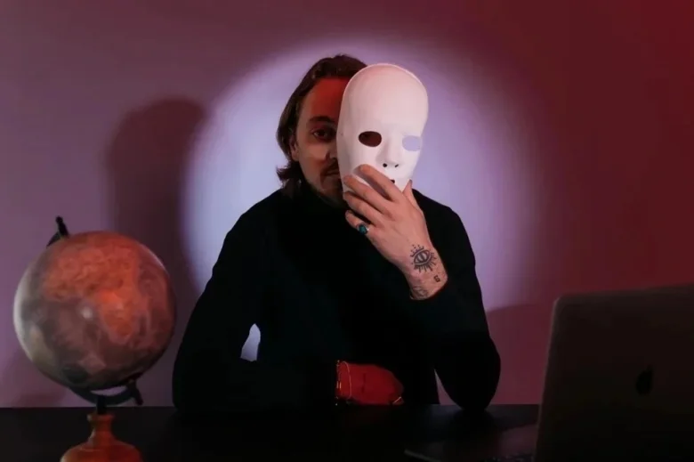 Muž s bílou maskou u globusu na stolu.