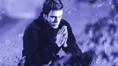 Muž sedí v trávě s dlaněmi spojenýma jako by si vzpomínal.