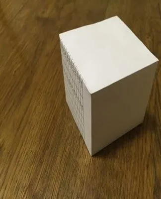 Bílá kostka z papíru nebo lepenky na dřevěném povrchu.