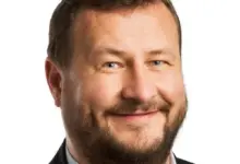 Portrét usměvavého muže v obleku na bílém pozadí.