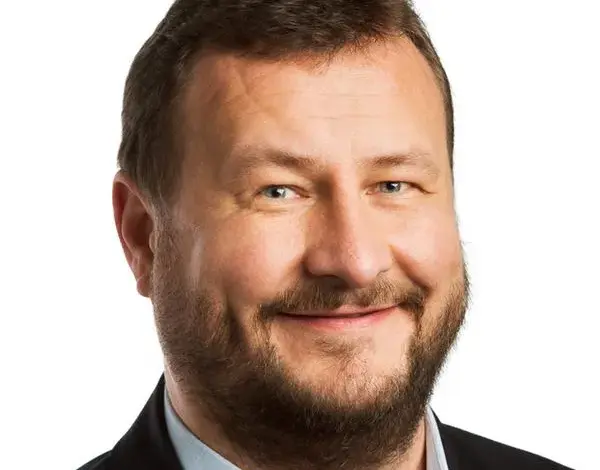 Portrét usměvavého muže v obleku na bílém pozadí.