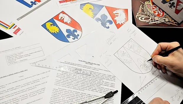Ruka kreslí erb s lva na papíru mezi dokumenty o symbolice barev.