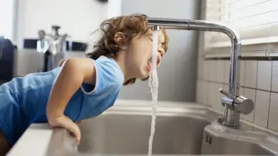 Dětský chlapec pije vodu z kohoutku na kuchyňské dřezu.