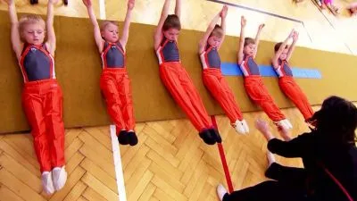Děti ve výcviku gymnastiky visí na paralelních lištách.