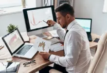 Muž analyzuje grafy produktivity na monitorech v kanceláři.