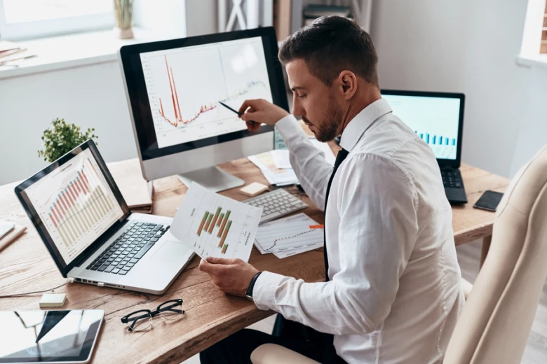 Muž analyzuje grafy produktivity na monitorech v kanceláři.