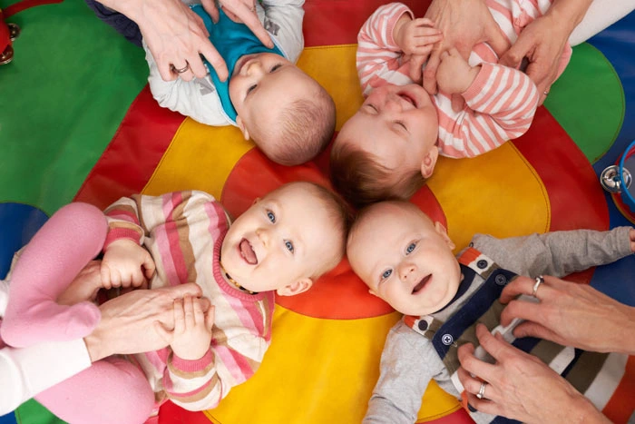 Čtyři usměvavá miminka leží na barevné hrazdě s dospělými.